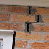 A brick wall displaying stair-step cracks and messy tuckpointing on a Lewiston home