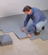 Contractors installing basement subfloor tiles and matting on a concrete basement floor in Dover, Maine